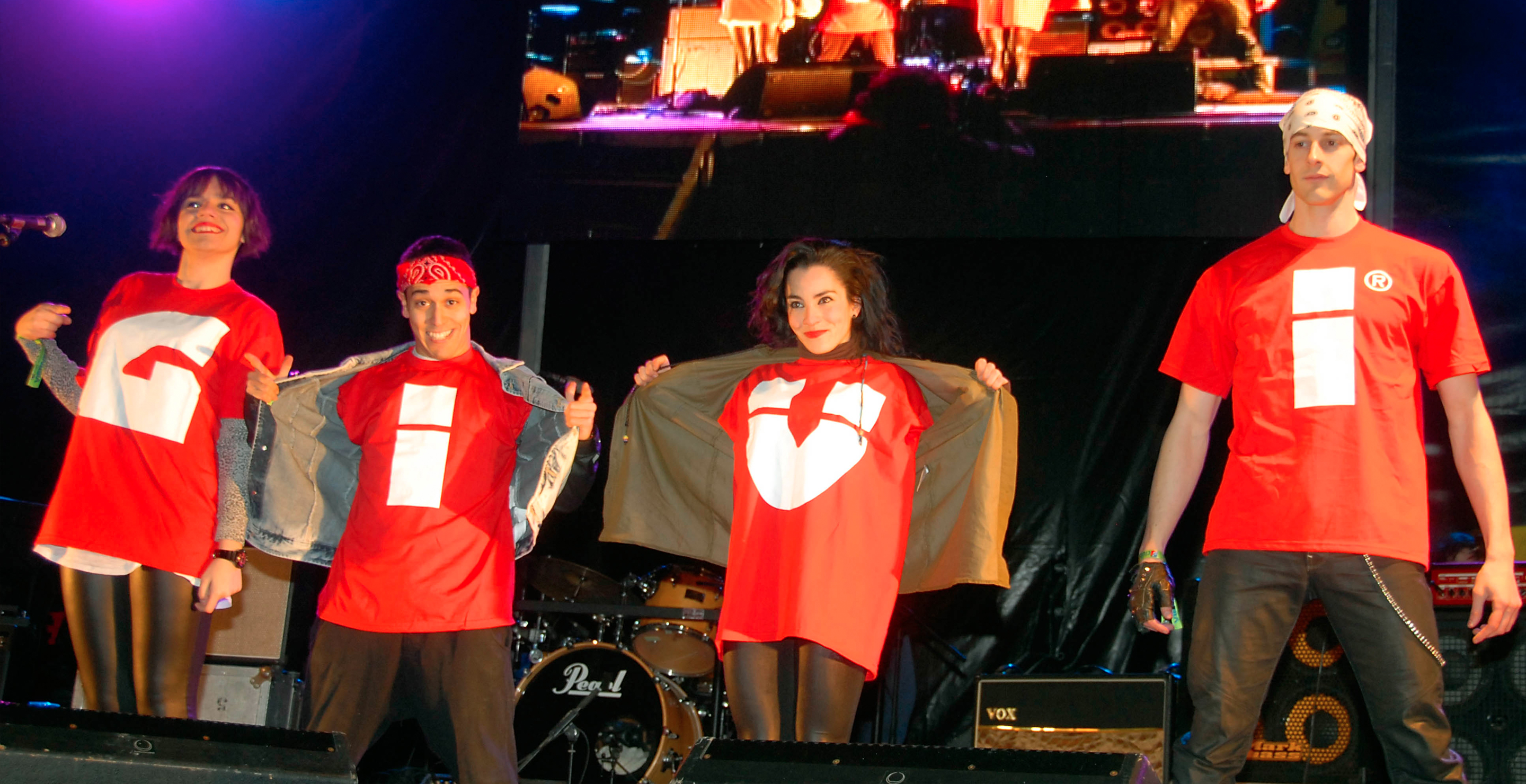 Personas sobre escenario mostrando sus camisetas formando el logotipo de GIVI